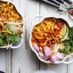 Two bowls of Khao Soi garnished with cilantro, lime, and red onions.