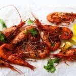 Grilled prawns with herbs and lemon wedges on parchment paper.