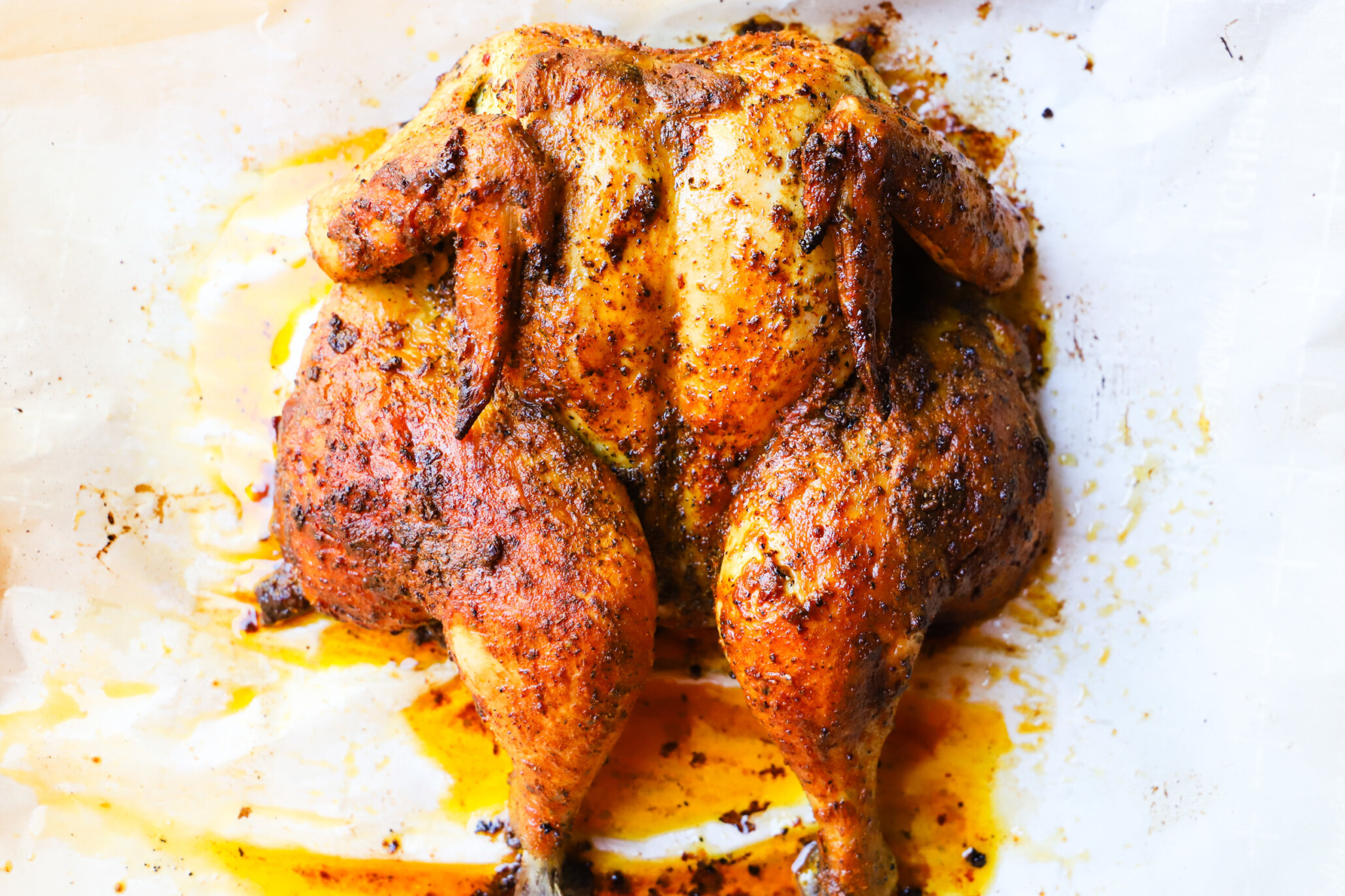 Spatchcock chicken seasoned with paprika and mustard on parchment paper.
