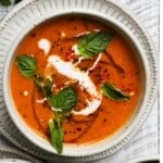 A bowl of roasted tomato basil soup with cream and fresh basil garnish.
