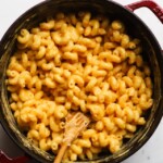 Creamy macaroni and cheese in a pot with a wooden spoon.