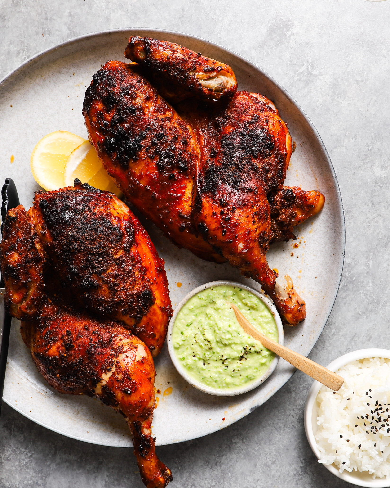 Grilled chicken with a spicy crust, dip, lemon slices, and rice.