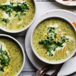 Bowls of creamy broccolini soup garnished with broccolini and cheese on a table.