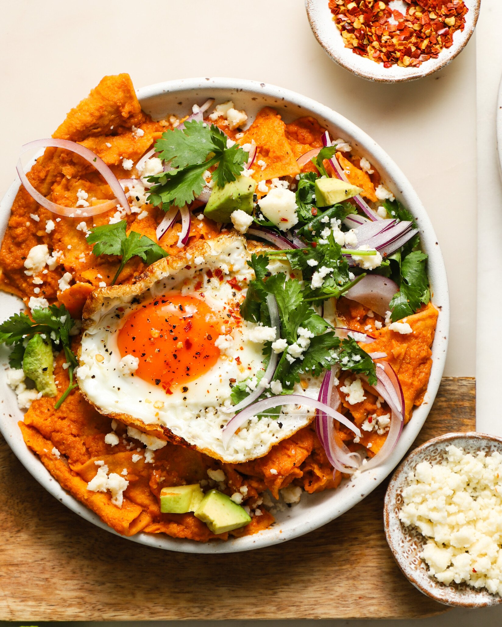 A plate of chilaquiles topped with a fried egg, avocado, and cilantro.
