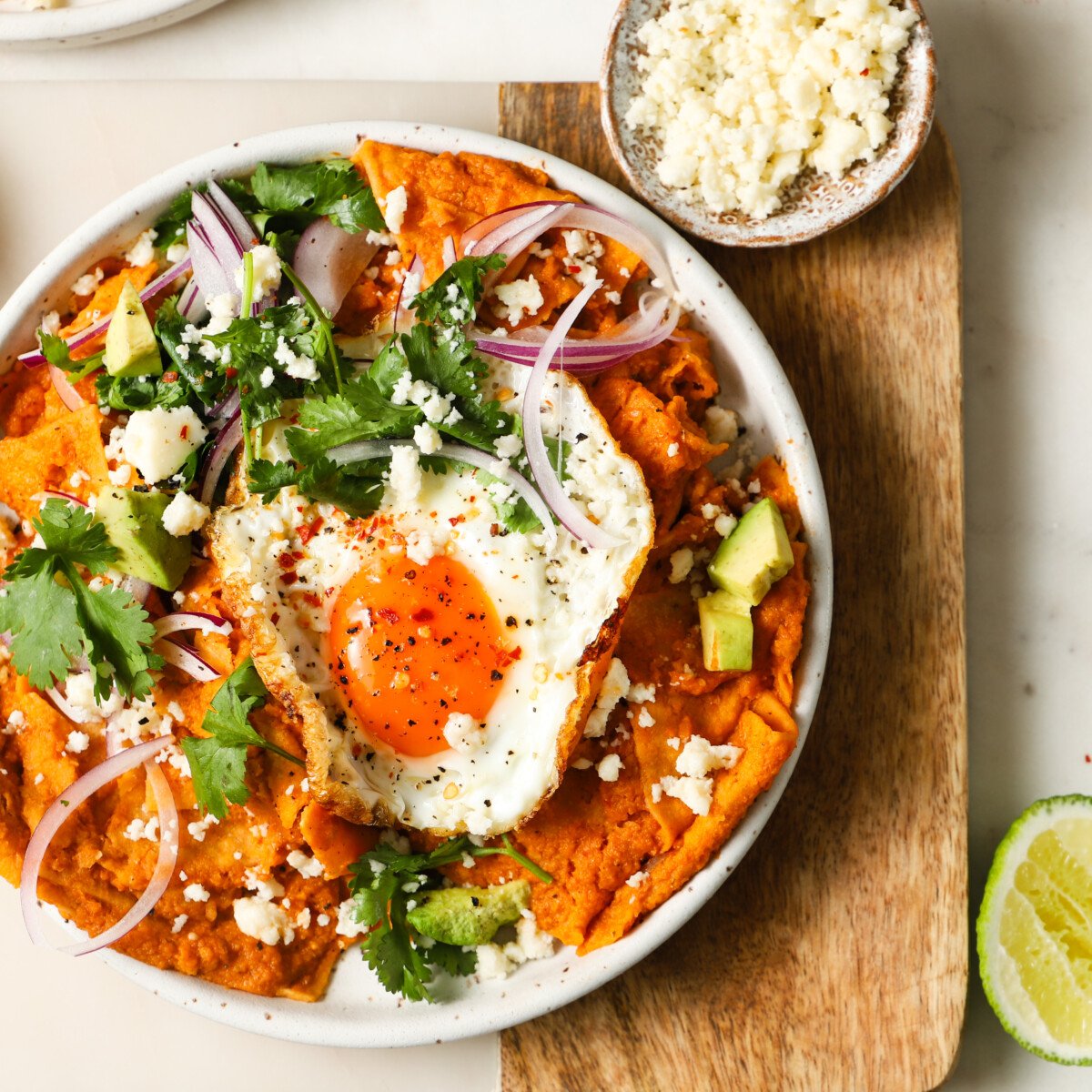 Plate of chilaquiles with fried egg, avocado, onions, cilantro, and crumbled cheese.
