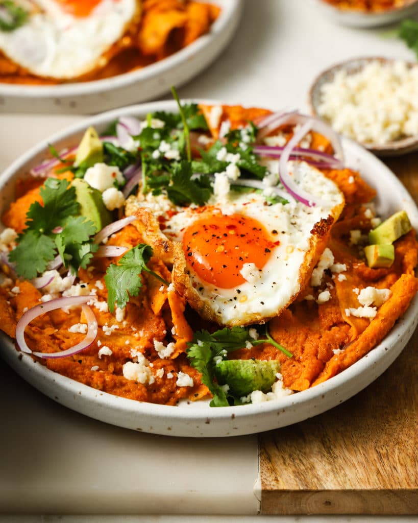 Chilaquiles topped with a fried egg, avocado, red onions, cilantro, and cheese.