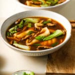 Bowl of potsticker soup with bok choy and mushrooms, garnished with green onions.