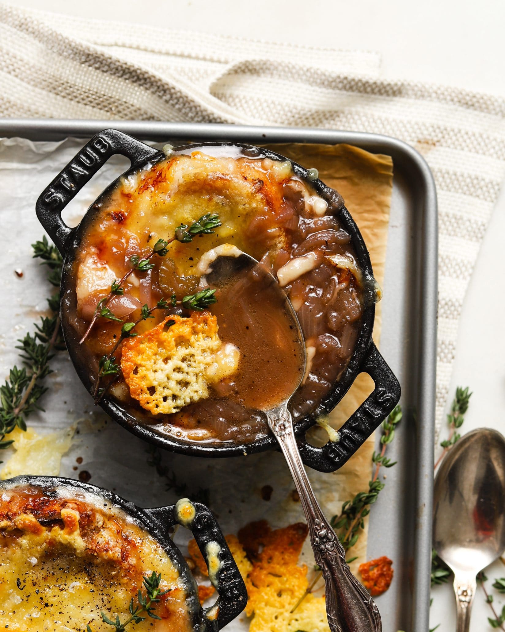 French onion soup in a black pot with melted cheese and thyme garnish.