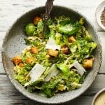 Fresh Brussels sprouts Caesar salad with croutons and shaved Parmesan in a bowl.