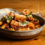 Bowl of rigatoni with lamb ragu, topped with parsley and grated cheese.