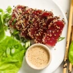 Seared ahi tuna with sesame seeds, lettuce, scallions, and dipping sauce on a plate.