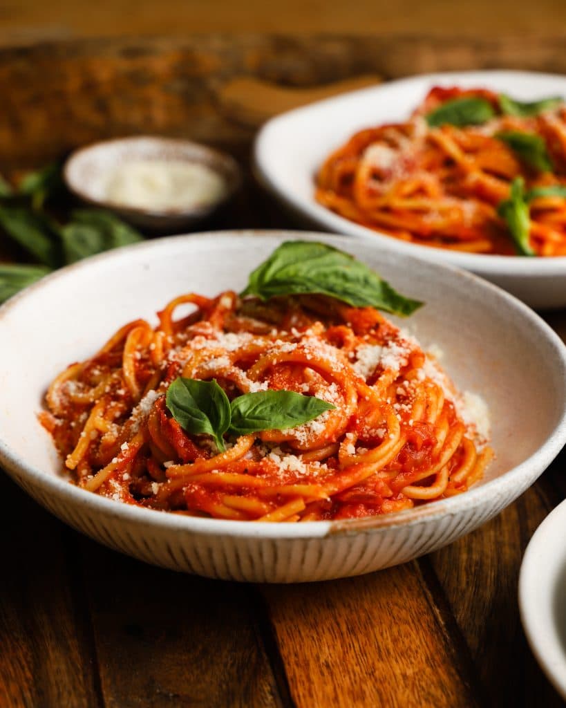 Pasta with roasted tomato sauce, garnished with basil and parmesan, in a white bowl.