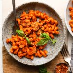 A bowl of curly pasta with tomato sauce, basil, and red pepper flakes.