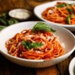 A bowl of spaghetti pomodoro garnished with basil leaves and grated cheese.