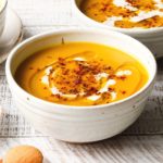 A bowl of creamy butternut squash soup with seasoning and drizzle on top.