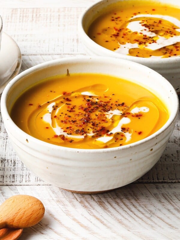 A bowl of creamy butternut squash soup with seasoning and drizzle on top.