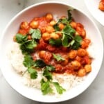 A bowl of rice topped with chickpeas in tomato sauce and cilantro.