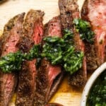 Grilled steak slices topped with vibrant green chimichurri sauce on a wooden board.