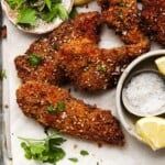 Crispy chicken schnitzel garnished with parsley, sesame seeds, and lemon wedges.