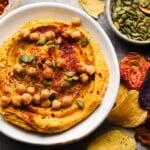 Bowl of sweet potato hummus topped with chickpeas and seeds, surrounded by chips.