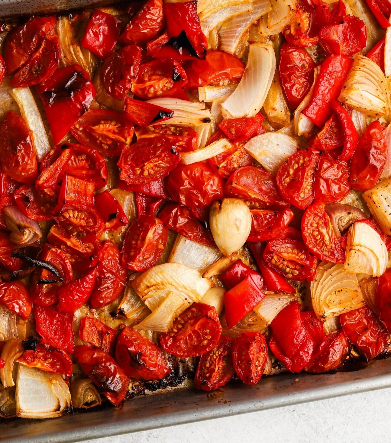 Roasted onions, tomatoes, and bell peppers on a baking sheet.
