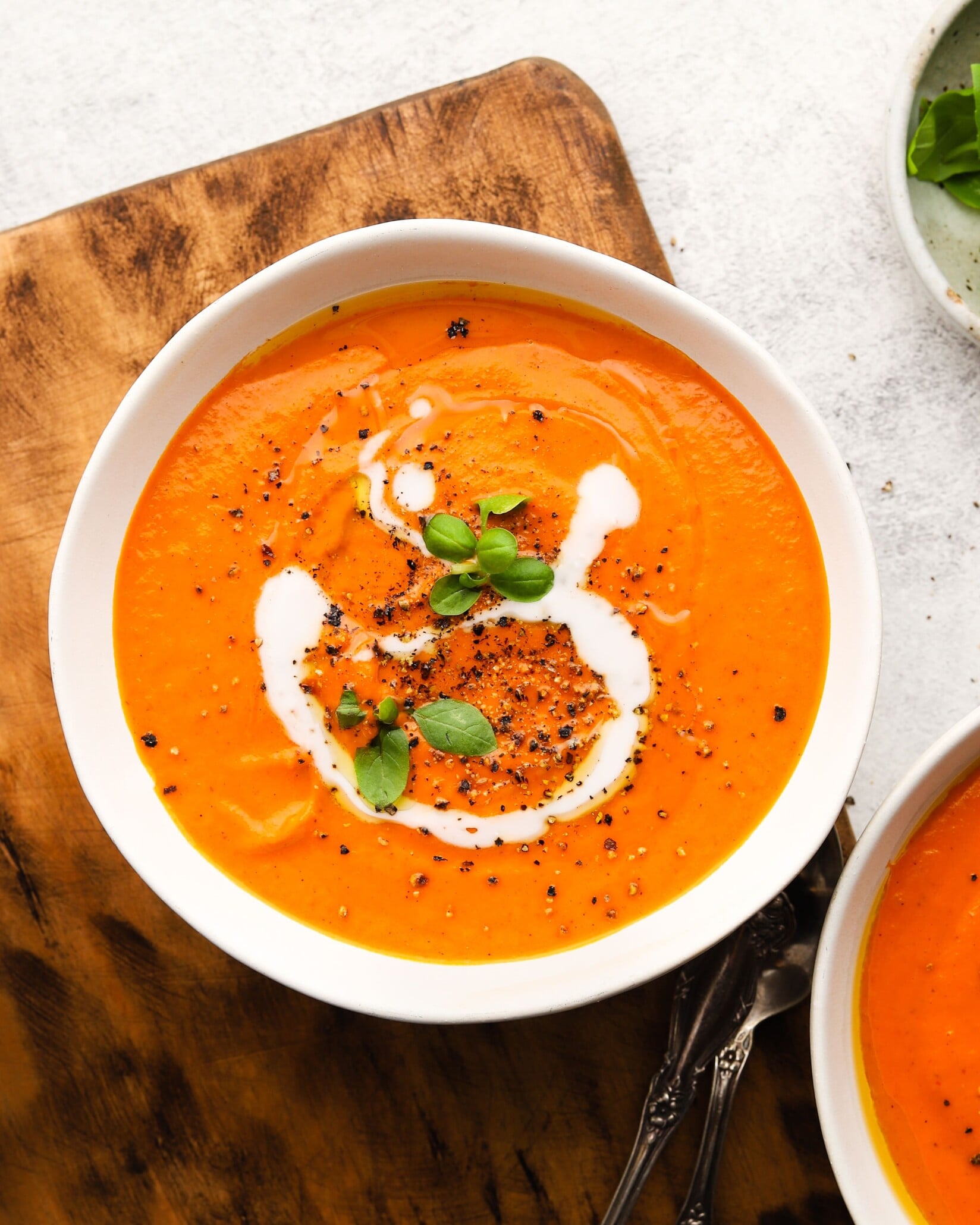 Bowl of creamy tomato soup topped with black pepper, cream, and fresh basil.