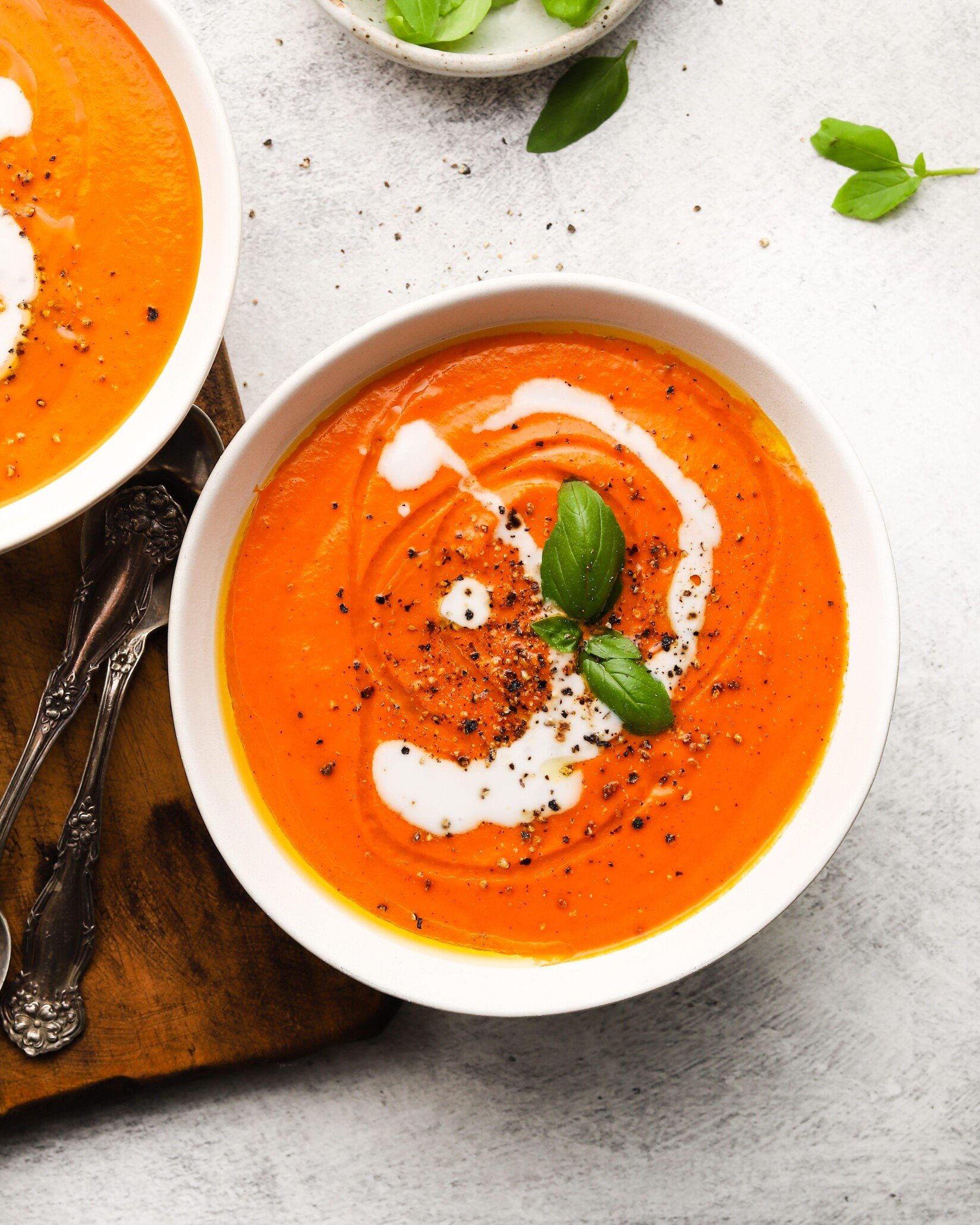 Bowl of roasted red pepper and tomato soup garnished with cream and basil.