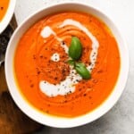Creamy red pepper tomato soup garnished with basil and black pepper.