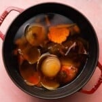 Pot filled with onions, garlic, and vegetables soaking in water for broth preparation.