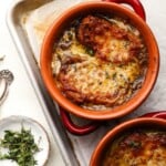 Two bowls of baked vegetarian French onion soup garnished with fresh thyme.