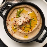 Creamy mushroom soup garnished with rosemary, pepper flakes, and olive oil in a dark bowl.