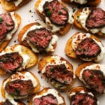 Sliced steak on crostini with burrata and chives, arranged on a white plate.