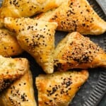 Golden puff pastry triangles topped with sesame seeds on a dark plate.