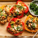 Stuffed red and yellow peppers with tuna, orzo, cheese, and fresh herbs on parchment.