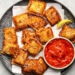 Crispy toasted ravioli with marinara sauce and a lemon wedge on a plate.