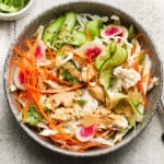 Colorful chicken salad with sesame dressing, cucumber, radish, carrot, and cabbage in a bowl.