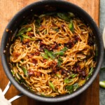 Stir-fried ramen noodles with vegetables and sesame seeds in a black pan.