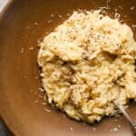 Creamy orzo pasta with grated cheese and black pepper in a brown bowl.