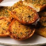 Slices of golden, crispy garlic bread garnished with herbs on a white plate.
