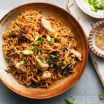 Bowl of chicken ramen noodles with scallions, sesame seeds, and chili flakes.
