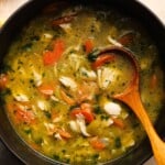 A pot of chicken orzo soup with carrots and herbs, stirred with a spoon.