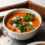 A bowl of tomato lentil curry topped with fresh cilantro and cream.