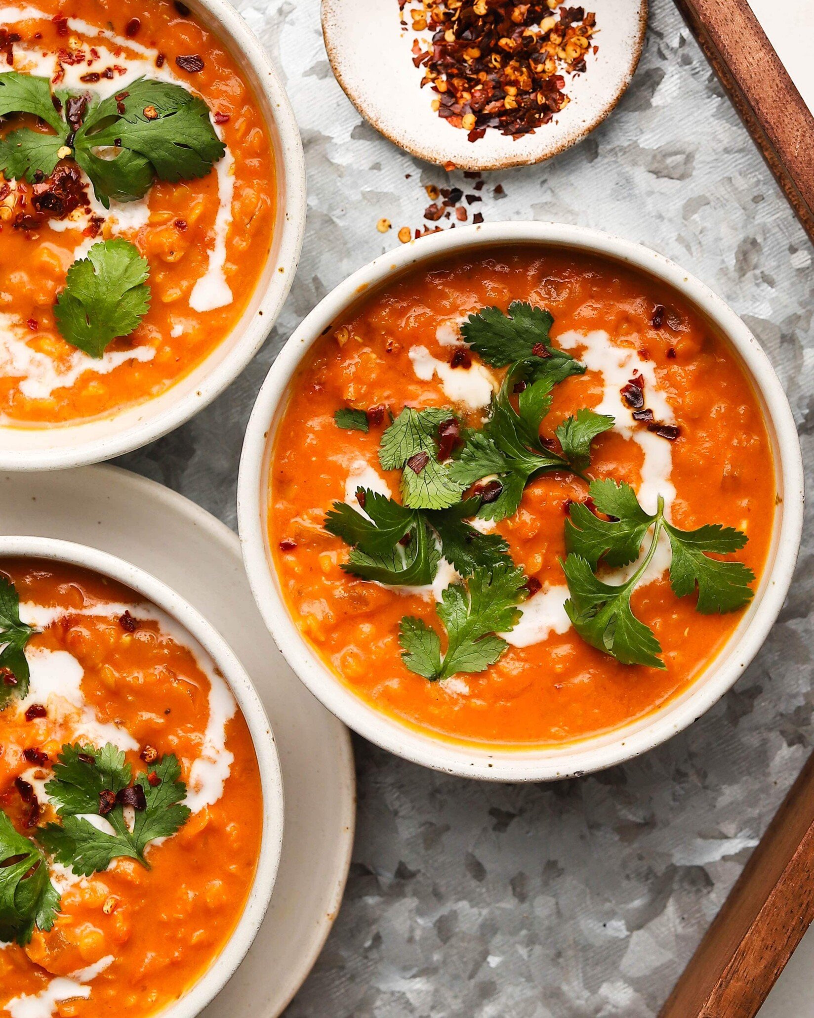 Bowls of vibrant lentil tomato curry garnished with cilantro and served with spices.