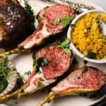 Rack of lamb with herbs, turmeric couscous, fresh greens, and seasoning on a plate.