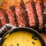 Sliced steak with peppercorn crust and Béarnaise sauce on a wooden board.