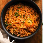 Spicy ramen topped with egg yolk, sesame seeds, and green onions in a bowl.