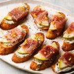 Toasts topped with pear, prosciutto, and Gorgonzola, garnished with black pepper and zest.