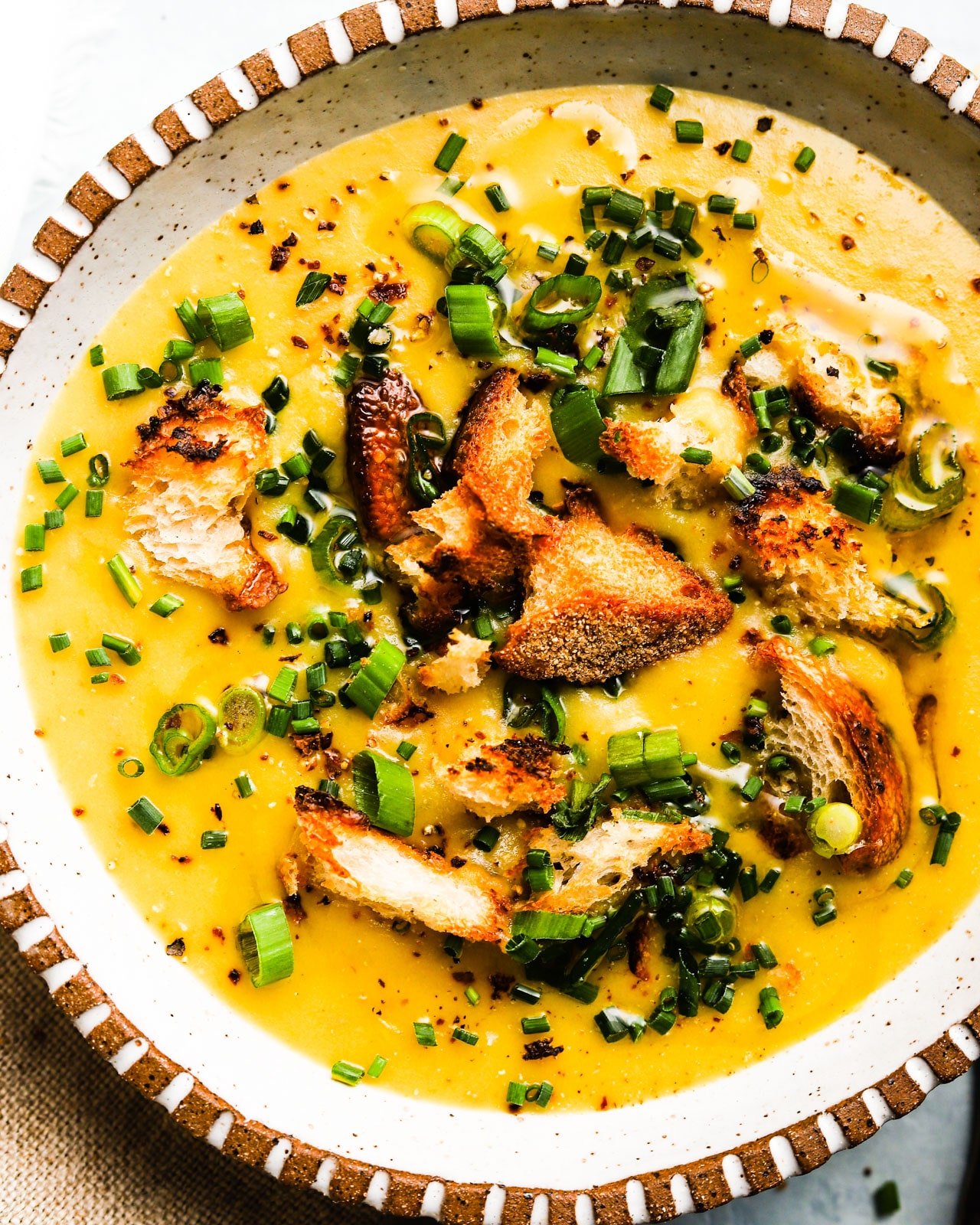 Creamy soup topped with croutons and chopped green onions in a decorative bowl.