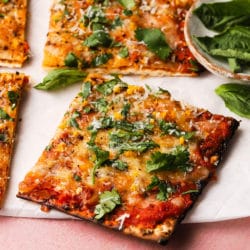 A slice of matzo pizza topped with cheese, cilantro, and herbs on parchment.