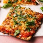 A slice of matzo pizza topped with cheese, cilantro, and herbs on parchment.
